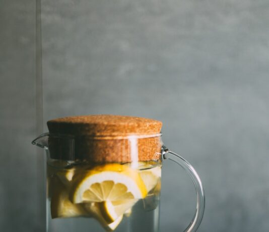 여름철 체력 유지와 정신 건강 관리법 clear glass pitcher filled with sliced lemons on black and white table runner