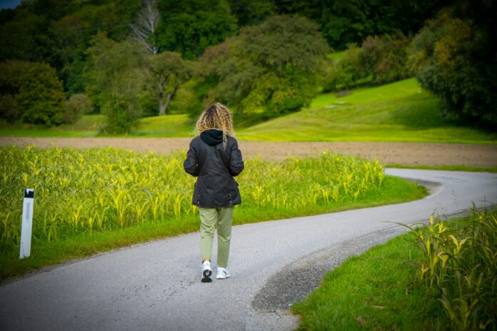 Woman walking on a winding road through fields.