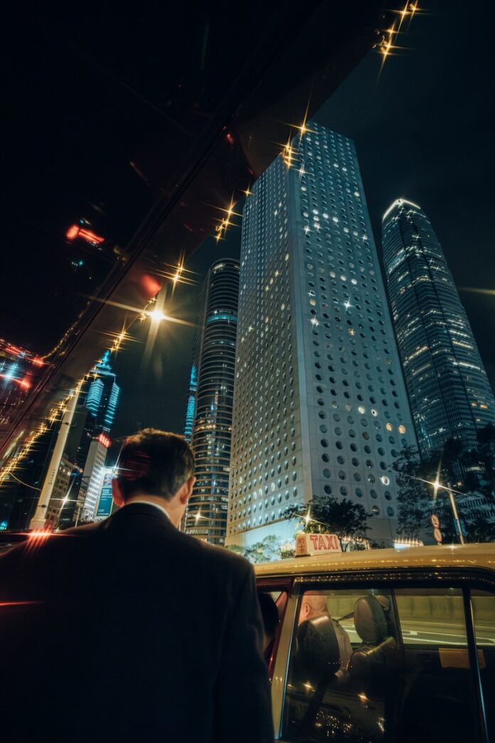 Man in suit enters taxi with city skyscrapers at night